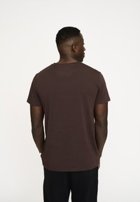 Brun kortærmet t-shirt med rund hals, let materiale og en glat tekstur, set fra ryggen.