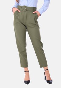Pantaloni verdi oliva con vita a cintura, fronte plissettato e tasche laterali. Tessuto morbido, design cropped, abbinati a tacchi a punta neri.