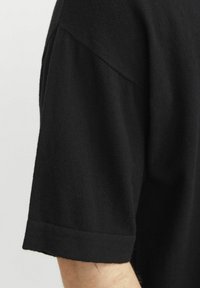 Camisa negra de manga corta con una textura suave, corte holgado y puños enrollados. La tela parece ligera y suave.