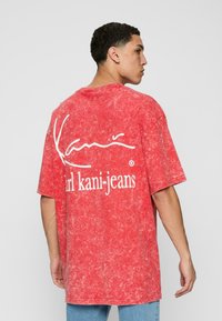 Red oversized t-shirt with a marbled texture. Features white logo text on the back. Short sleeves and a classic crew neckline.