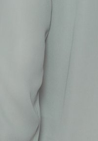 Blusa azzurra chiara con una texture liscia e leggermente trasparente. Presenta una vestibilità morbida e dettagli delle cuciture sottili lungo le maniche. Tessuto morbido e fluente.