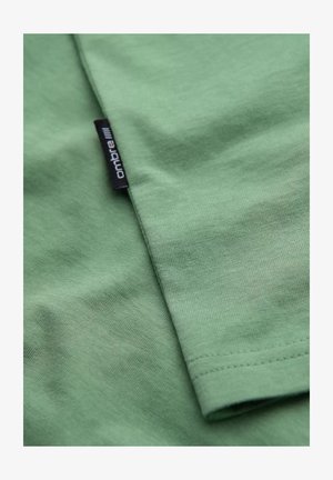 Zielona bawełniana koszulka z gładką strukturą i metką przyszytą do brzegu. Prosty design z miękkim wykończeniem.