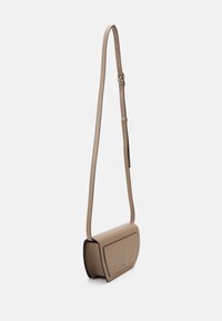 Bolso de cuero beige tipo bandolera con forma curvada, correa desmontable y diseño minimalista. Presenta una textura suave y un logo sutil.