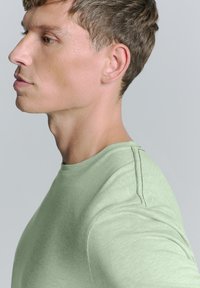 Lichtgroene t-shirt met korte mouwen, ronde halslijn, met een gestructureerde stof, voorzien van contrasterende stiksels langs de schoudernaad.