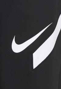 Gros plan sur un tissu noir avec le logo Nike Swoosh blanc et un détail de bande blanche inclinée sur le côté droit.