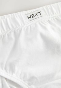 Culotte en coton blanc avec une ceinture élastique. Présente une étiquette avec "NEXT" imprimée en noir. Texture lisse et design simple.