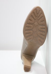 Chaussure à talon haut beige avec une semelle texturée, présentant un design contour et un talon strié. La semelle extérieure affiche une adhérence à motif pour la traction.