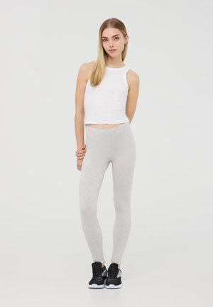 Leggings grigio chiaro realizzati in un tessuto morbido ed elastico, abbinati a un top aderente bianco e scarpe da ginnastica nere. Texture liscia e vestibilità slim.