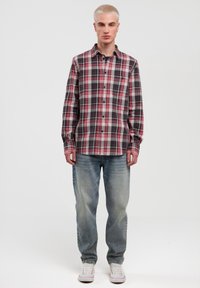 Tjekket flannel skjorte med røde, sorte og hvide mønstre, lange ærmer, knap-up design, parret med falmede blå jeans og hvide sneakers.