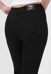 Zwarte denim jeans met een slim-fit ontwerp, voorzien van twee achterzakken en een merketiket op de tailleband. Gladde textuur en stevige stiksels.