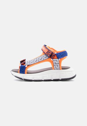 Sporty sandal with thick white sole, orange straps, blue and gray geometric patterned fabric, and Velcro closures.