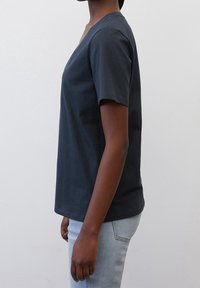 Mørkegrå bomulds T-shirt med korte ærmer, v-udskæring, afslappet pasform og glat tekstur. Båret med lyseblå jeans, vist fra siden.