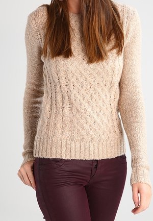 Beige gestrickter Pullover mit einem strukturierten Zopfmuster, Rippbündchen und Saum, kombiniert mit dunkelburgunderfarbene, eng anliegende Hose.