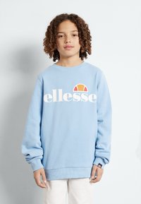 Sudadera azul clara con mangas largas y cuello redondo. Presenta un logo blanco con un acento en rojo y naranja. Tejido suave y texturizado.
