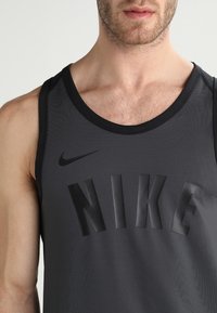 Canottiera sportiva nera con grande logo "NIKE" in rilievo sul davanti, realizzata in materiale leggero e texture, con scollatura rotonda.
