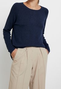 Maglione a maglia blu navy con maniche lunghe e scollo rotondo, abbinato a pantaloni beige a pieghe. Tessuto liscio e vestibilità comoda.