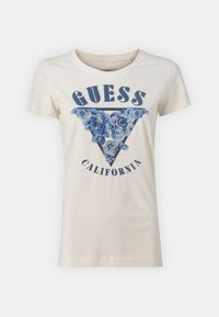 Camiseta de algodón blanca con un gráfico triangular floral azul y el texto "GUESS CALIFORNIA" debajo en azul oscuro, con cuello redondo y mangas cortas.
