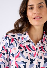 Blusa con colletto in tessuto leggero, caratterizzata da un motivo floreale nei colori rosa, rosso, blu navy e viola chiaro. Chiusura con bottoni sul davanti e vestibilità comoda.