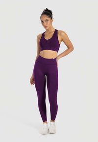 Top deportivo morado y leggings a juego hechos de un tejido elástico que absorbe la humedad. Presentan un diseño de espalda cruzada y una cintura alta.
