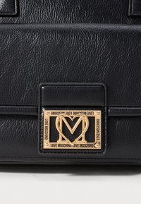 Fekete textúrájú bőrtáska arany fém logóval, amelyen a "LOVE MOSCHINO" felirat és egy szív alakú minta található az "M" körül.