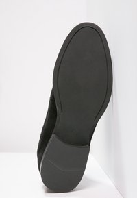 Black suede shoe with a textured upper, flat rubber sole, and a marked size "39" visible on the sole’s surface.