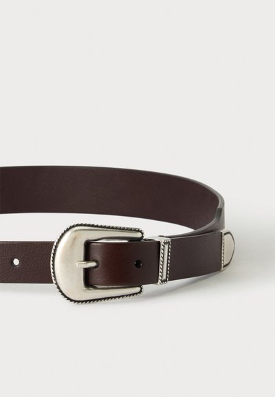 Ceinture en cuir brun foncé avec une boucle argentée de style western et des ornements métalliques décoratifs sur un fond uni.