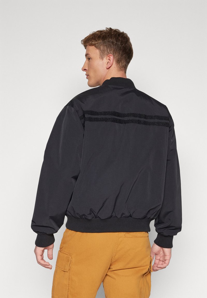 Czarna kurtka bomberka o luźnym kroju, z prążkowanymi mankietami i kołnierzem. Posiada poziome czarne paski na plecach oraz elastyczny dół.