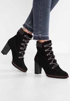 Sorte ankelstøvler i ruskind med chunky hæl, snørebånd foran og metalhardware. Har teksturerede sidepaneler og gummisål for greb.