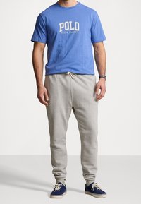 Modrá bavlněná tričko s logem "POLO RALPH LAUREN" v kombinaci se světle šedými teplákovými kalhotami a tmavě modrými teniskami s bílou podrážkou.