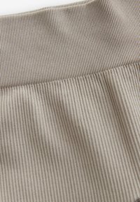 Tessuto beige a coste con una finitura texturizzata e una cintura larga, che mostra righe verticali e una qualità morbida e elastica.