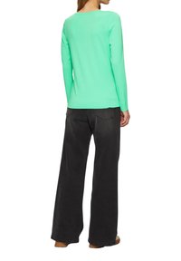 Zeleno-mint majica z dolgimi rokavi in okroglo ovratnikom, v kombinaciji z visokimi črnimi širokimi hlačami. Preprost dizajn in sproščen kroj.