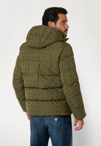 Green patterned puffer jacket with a hood, showcasing quilted sections and a smooth texture. Features a small logo at the back hemline.