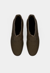 Bottines marron avec une texture en cuir lisse, des bords arrondis et un design minimaliste. Présente une ouverture supérieure inclinée sans quincaillerie visible.