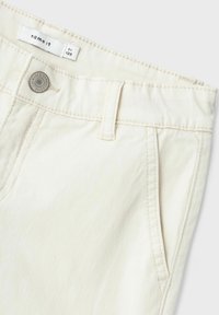 Pantalon en coton beige avec une fermeture à bouton, cinq poches et des coutures contrastées. Présente une étiquette portant la mention "name it" au niveau de la taille.