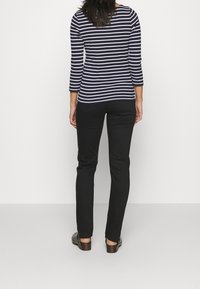 Camiseta de rayas azul marino y blanca de manga larga combinada con pantalones negros ajustados. El conjunto presenta un diseño clásico con un ajuste cómodo.