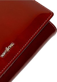 Portafoglio rosso lucido con texture liscia, dettaglio del logo dorato e cuciture ordinate lungo i bordi. Forma rettangolare compatta.