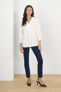 Witte blouse met lange mouwen en V-hals, gecombineerd met donker marineblauwe, slim fit broek en zwarte, elegante slingback hakken met puntige neus. Glad textuur van de stoffen.