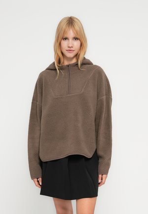Brauner Fleece-Pullover mit Kapuze, Frontreißverschluss bis zur Hälfte und übergroßem Schnitt. Mit strukturierter Stoffoberfläche und kontrastierendem Saumabschluss.
