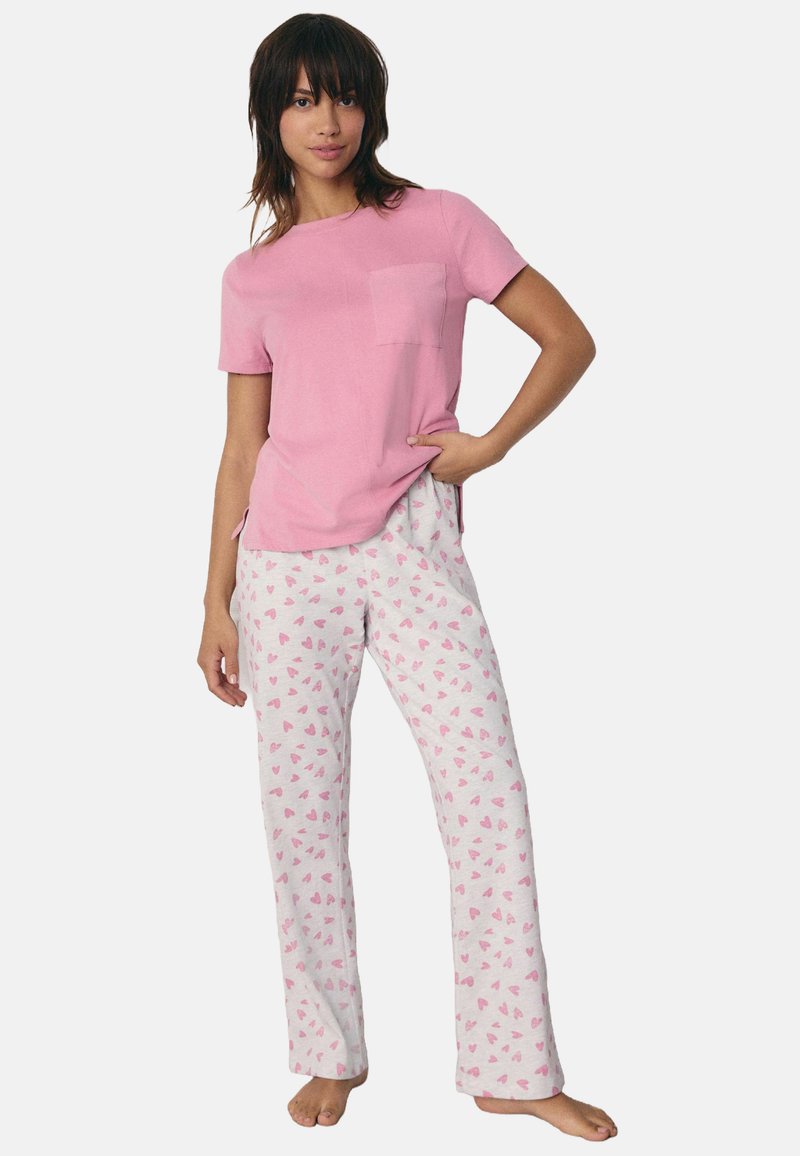 Roze katoenen T-shirt met een borstzak, gecombineerd met witte pyjamabroeken met een roze hartpatroon. Casual, ademende stof voor comfort.