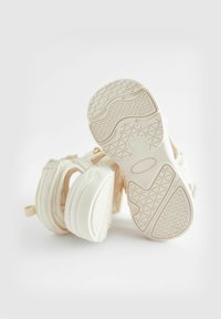 Baskets de couleur crème avec une semelle texturée, un design à plusieurs panneaux, un dessus en tissu doux et une languette à l'arrière pour un enfilage facile.