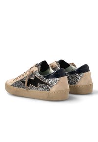 Zapatillas bajas de ante beige, con paneles de purpurina plateada, diseño de rayo negro y suelas de goma desgastadas, mostradas desde ángulos trasero y lateral.