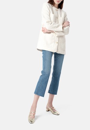 Hvid struktureret oversized jakke med to forlommer, parret med lyseblå cropped jeans og blanke guld block-heeled sko.