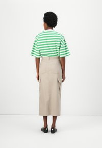 Haut à manches courtes rayé vert et blanc associé à une jupe beige mi-longue avec des poches cargo et une taille ceinturée. Chaussures noires.
