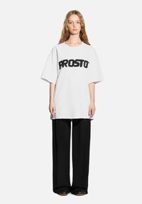 Biała, oversize'owa koszulka z czarnym logo "PROSTO", zestawiona z luźnymi czarnymi spodniami o swobodnym kroju i miękkiej fakturze.