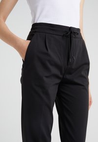 I pantaloni jogger neri presentano una vita elasticizzata con coulisse, tasche laterali e una superficie liscia. Adatti per un abbigliamento casual.