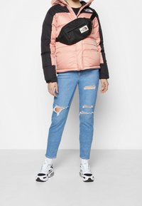 Padded jacket with pink and black sections, blue ripped jeans, a black waist bag, and white sneakers with black accents.