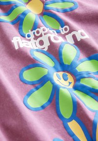 Lila Stoff mit leuchtend blauen und grünen Blumenmustern; in der Mitte befindet sich ein gelbes Smiley-Gesicht, umgeben von fettem weißen Text mit der Aufschrift "drop it to flatgram."
