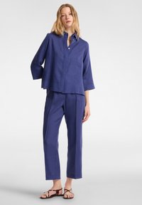 Completo due pezzi in lino blu scuro; presenta una camicia con bottoni a maniche tre quarti e pantaloni a gamba dritta. Sandali marroni e neri.