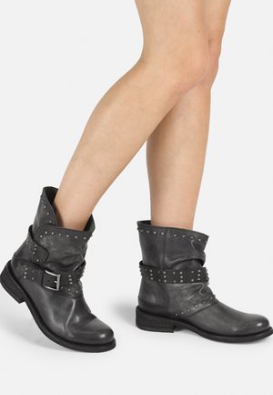 Botas de cuero negro hasta el tobillo con un diseño arrugado, acentos de tachuelas, una correa con hebilla y un tacón bajo de madera texturizada.