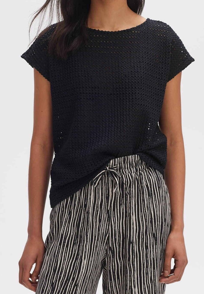 Top corto a maniche corte in maglia nera con scollatura rotonda, indossato con pantaloni a righe a vita alta con cintura regolabile.